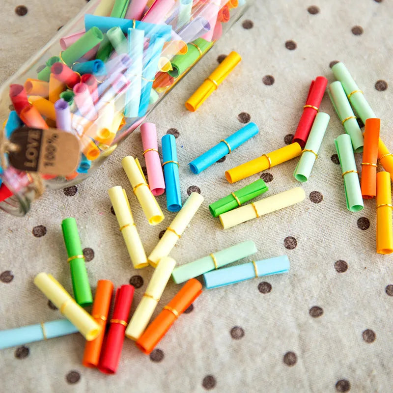 Assorted coloured mini paper scrolls with metal eyelets in sizes 3x7cm, 4x7cm, 5x5cm and 7x7cm.