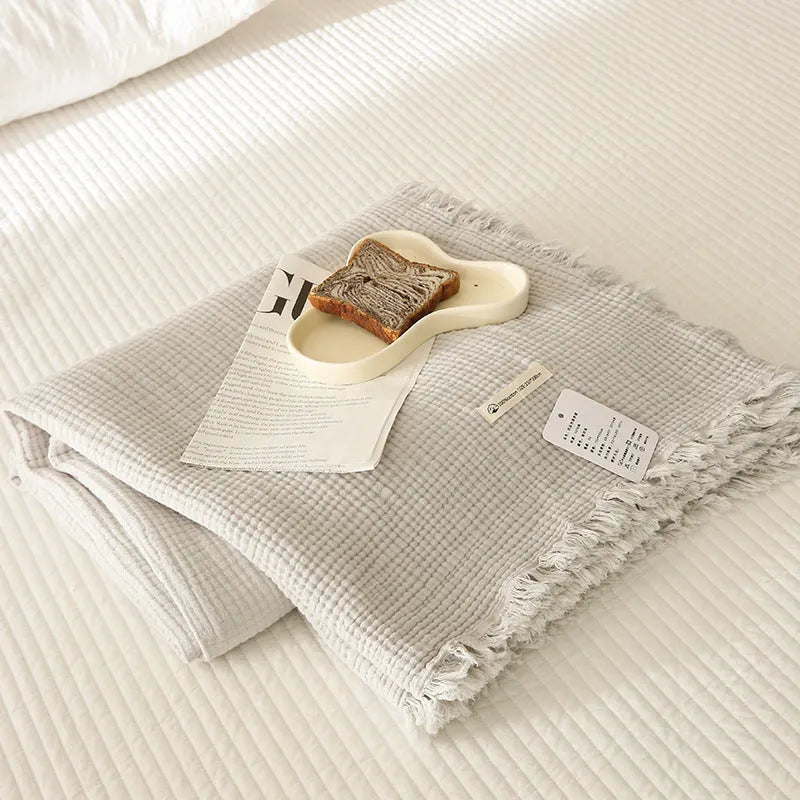 Four-layer cotton gauze blanket with tassel trim in avocado green colour laid flat.