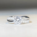 Silver ring with twisted arm design and a 1 karat moissanite stone in a four-claw setting.