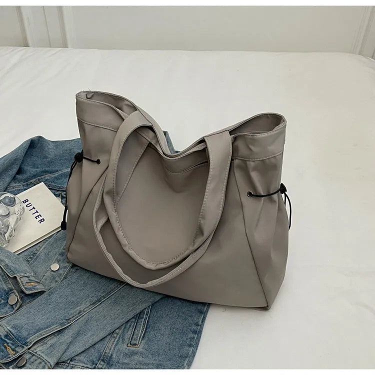 Soft Oxford cloth folding commuter tote bag shown in one of five colours: black, brown, dark grey, light grey or purple.