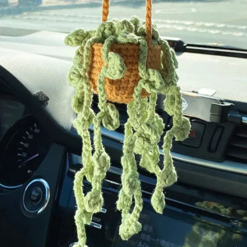 Green and white knitted wool car plant decoration hanging from a rope.