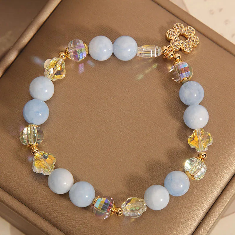 Women's aquamarine crystal bracelet with a four-leaf clover charm and pearl details on a white background