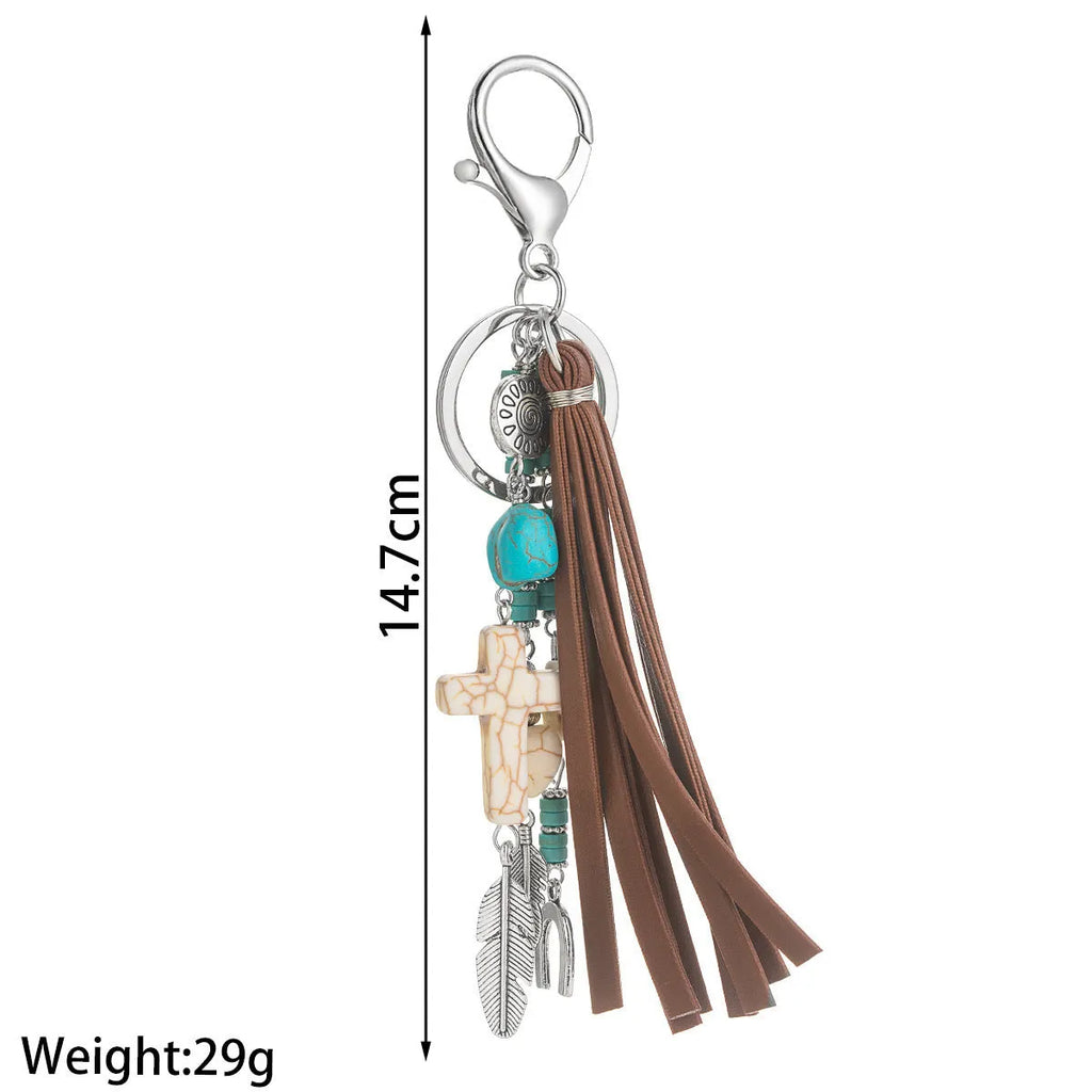 Alloy cross pendant keychain with leather rope and tassel in colour XY-3669 on a wooden surface