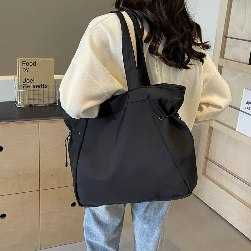 Soft Oxford cloth folding commuter tote bag shown in one of five colours: black, brown, dark grey, light grey or purple.