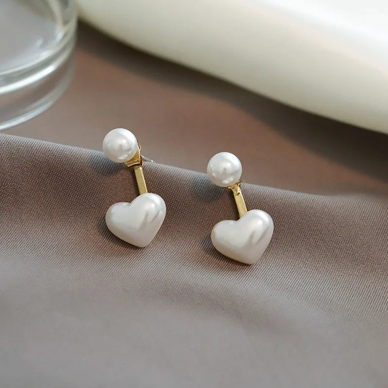 Close-up of women's silver-toned heart-shaped stud earrings with a central inlaid artificial pearl or gemstone.