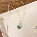 Women's necklace with coloured glaze joker pendant on a beige cotton and linen clavicle chain.