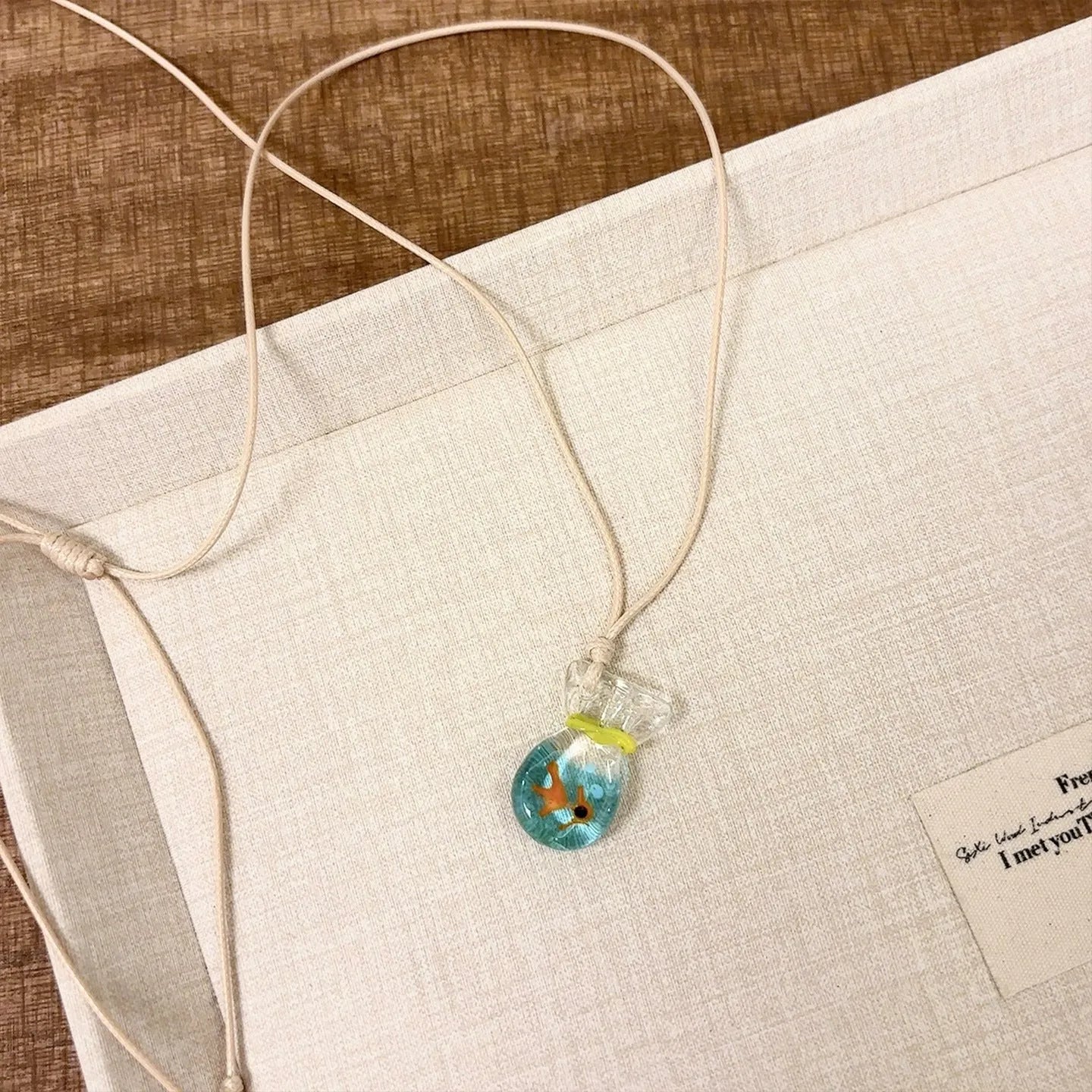 Women's necklace with coloured glaze joker pendant on a beige cotton and linen clavicle chain.