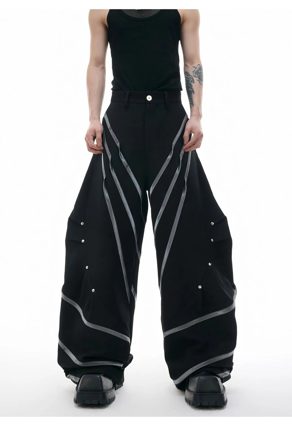 Men's black trousers with metal rivet pleats and a tapered leg, showing three-dimensional cutting.