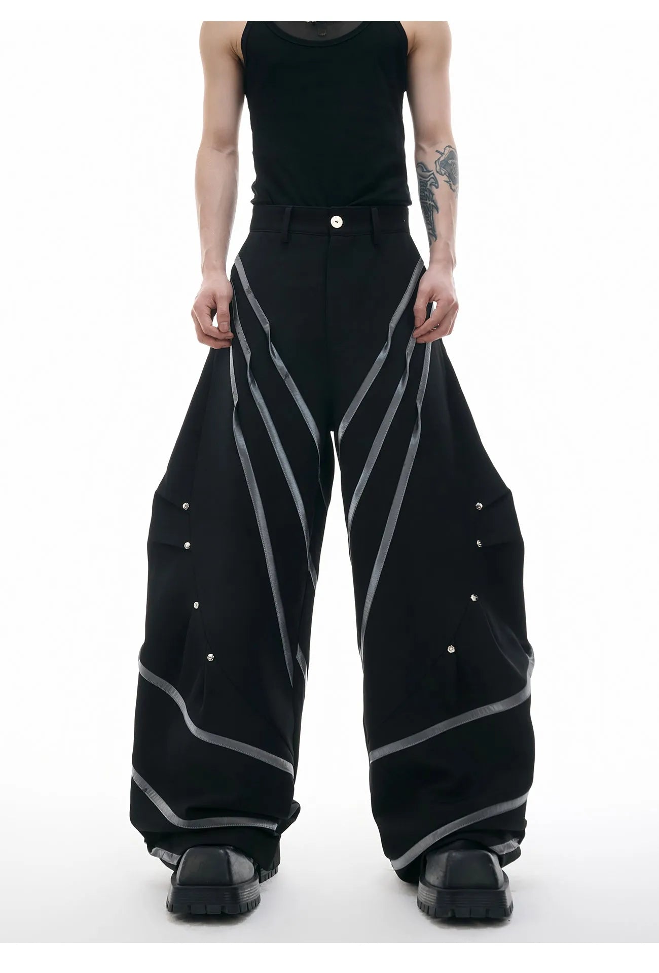 Men's black trousers with metal rivet pleats and a tapered leg, showing three-dimensional cutting.
