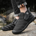 Men's black waterproof snow boot with thick sole and plush lining on a hard ground surface.