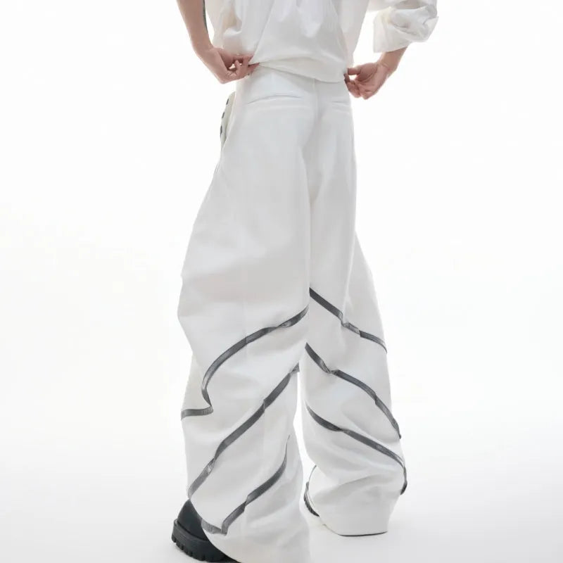 Men's black trousers with metal rivet pleats and a tapered leg, showing three-dimensional cutting.