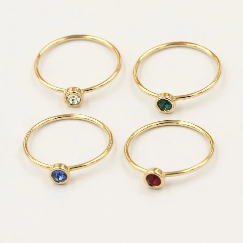 DIY knuckle ring craft kit showing 14K gold-plated ring base and green, blue, dark red, and white zircon accents.