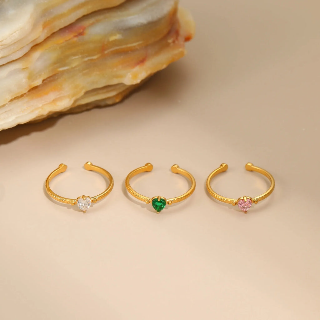Open-ended stainless steel ring with a geometric heart shape inlaid with green zirconium on a plain background.