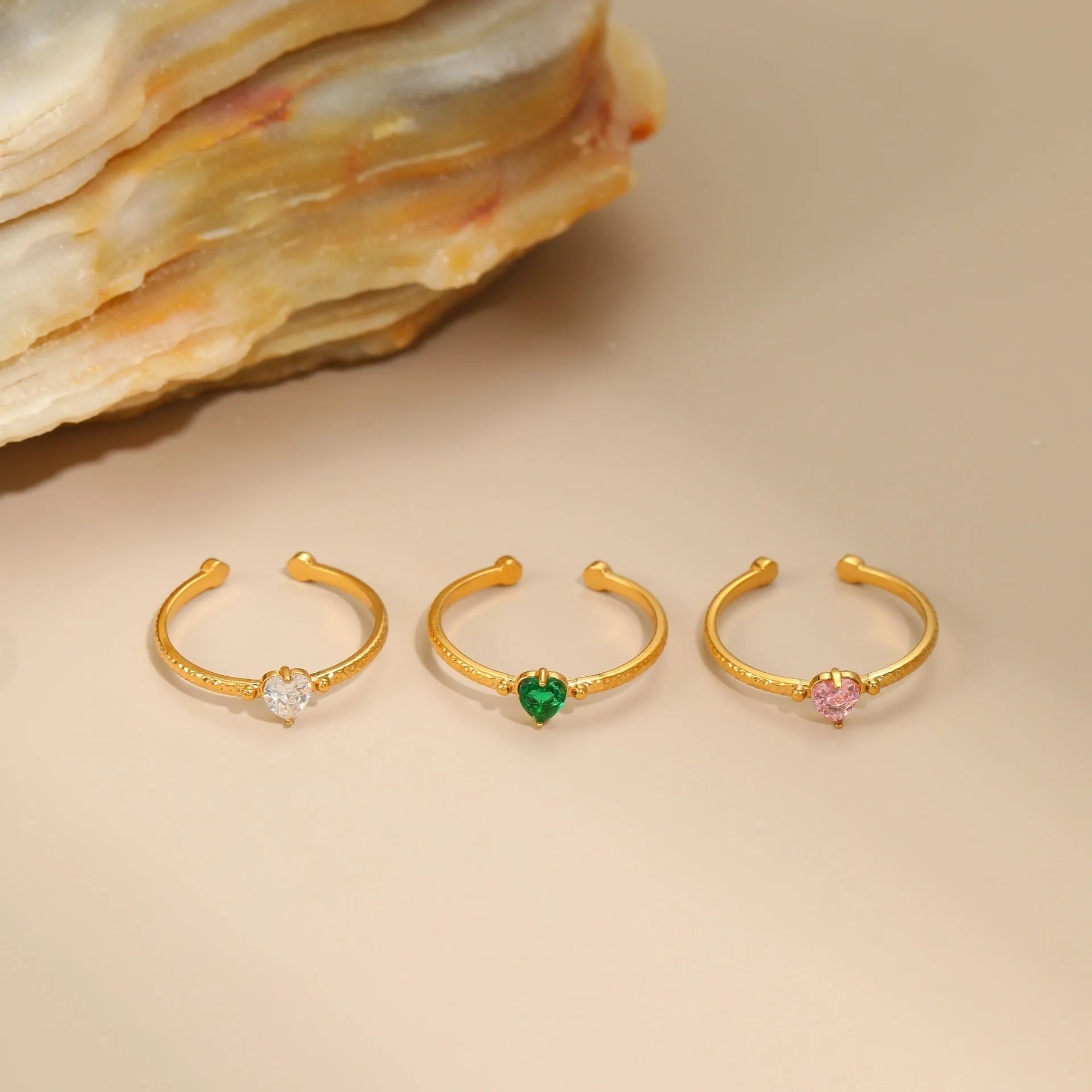 Open-ended stainless steel ring with a geometric heart shape inlaid with green zirconium on a plain background.