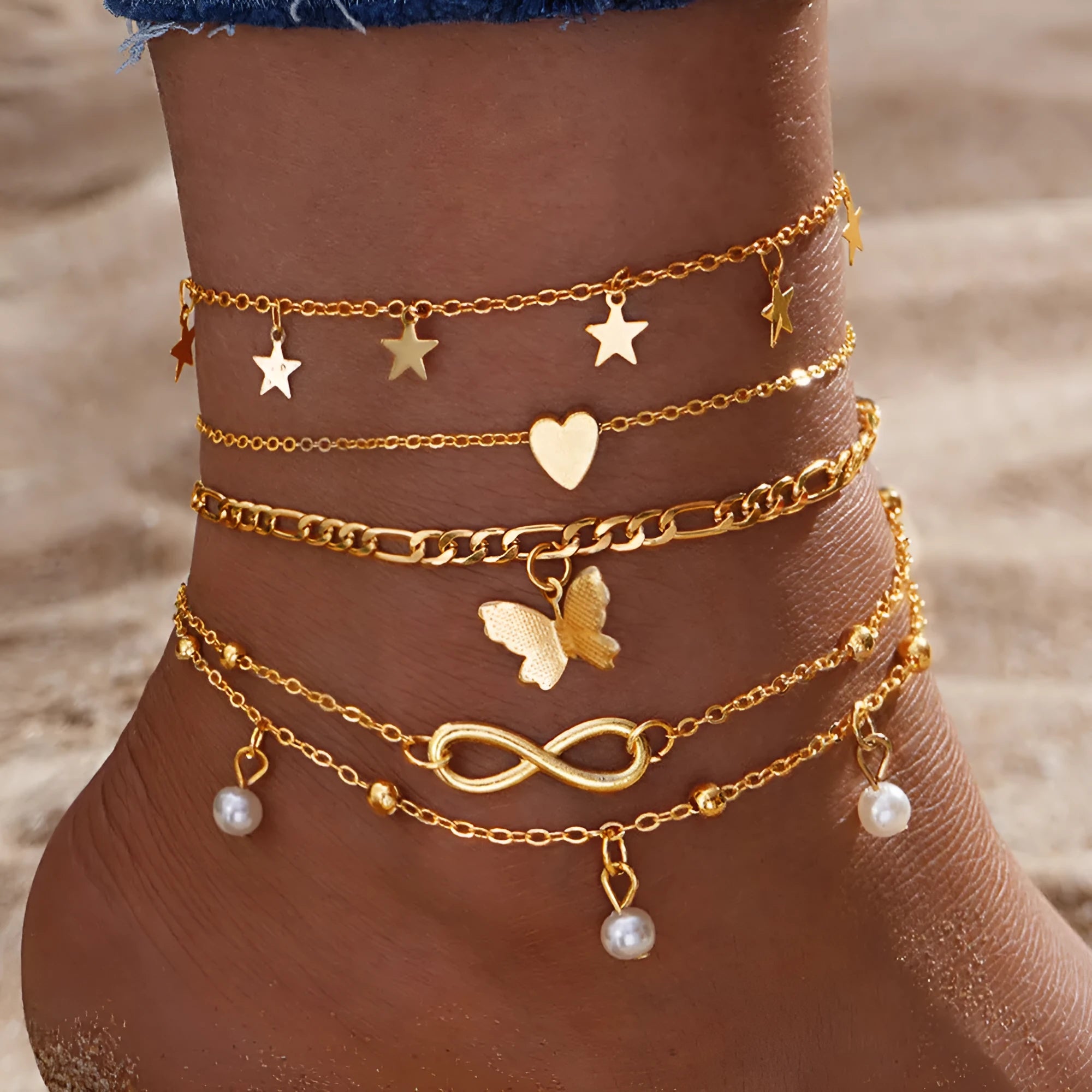 Four different alloy anklets with butterfly and pearl heart pendants arranged as a jewellery set
