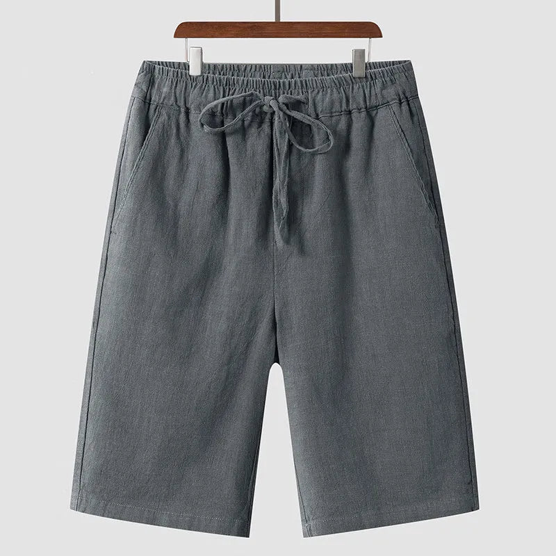 Men's beige linen casual shorts with loose cropped fit and elastic waistband on a neutral background.