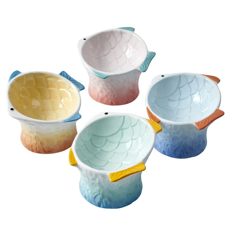 Set of four coloured fish-shaped ceramic cat bowls with a tilted, elevated design on a table.