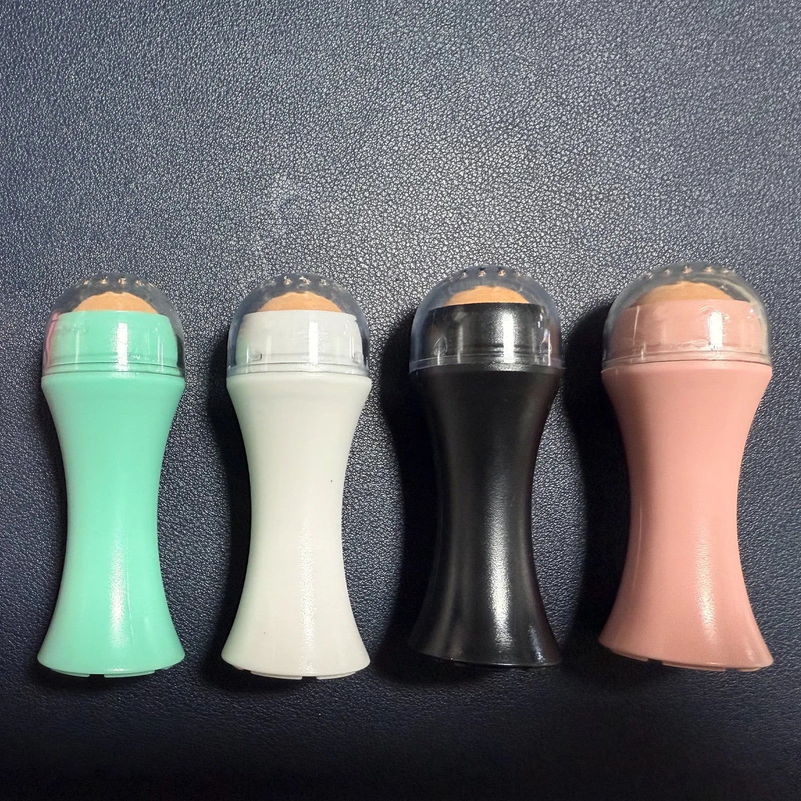 Volcanic stone facial roller in a plastic case for oily skin control, shown in one of four colours.