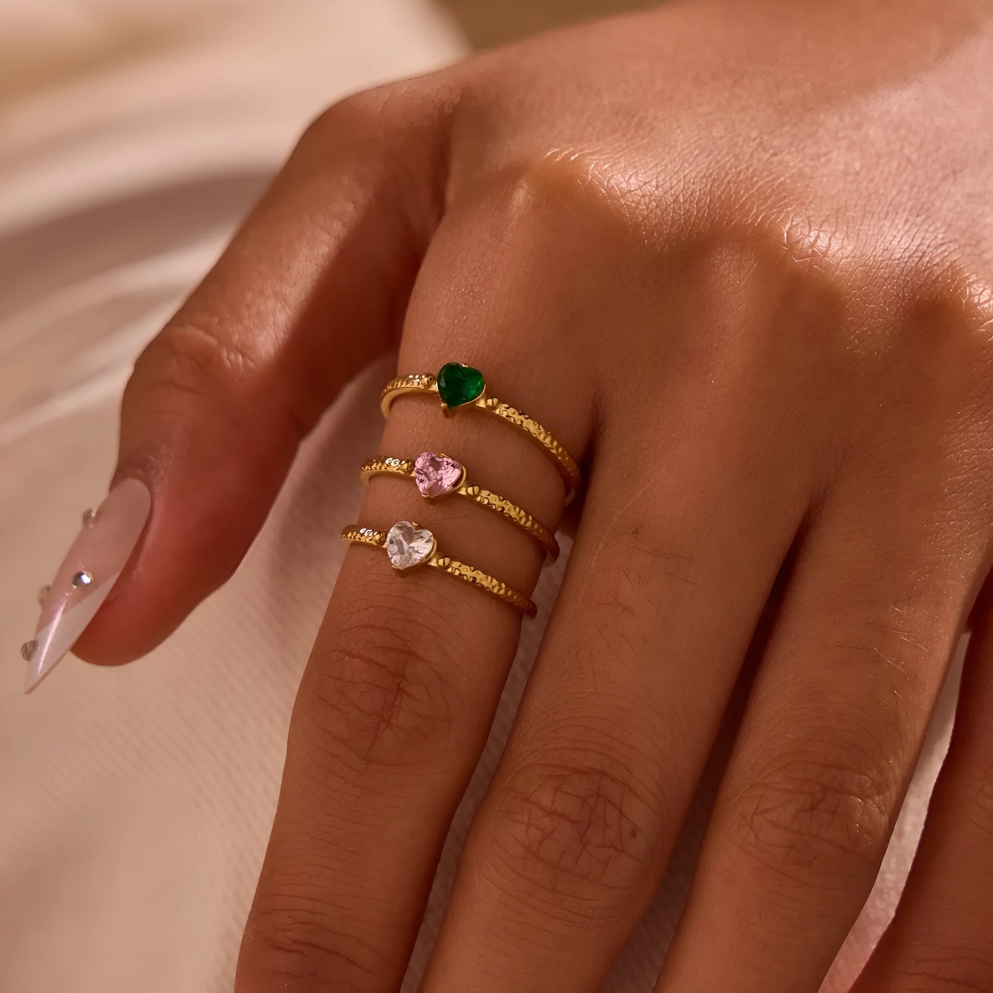 Open-ended stainless steel ring with a geometric heart shape inlaid with green zirconium on a plain background.