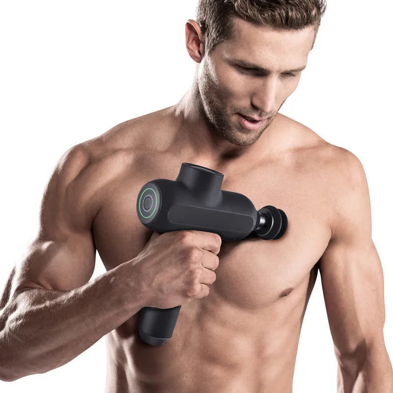 Handheld black electric muscle massager with six different massage heads on a table.