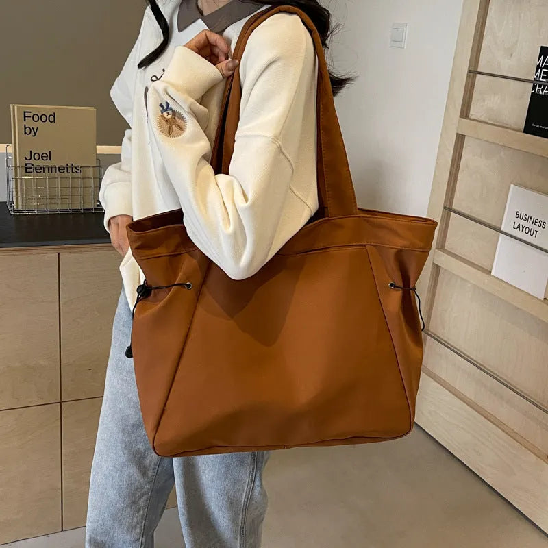 Soft Oxford cloth folding commuter tote bag shown in one of five colours: black, brown, dark grey, light grey or purple.