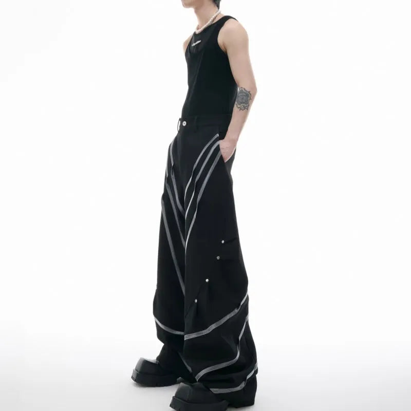Men's black trousers with metal rivet pleats and a tapered leg, showing three-dimensional cutting.