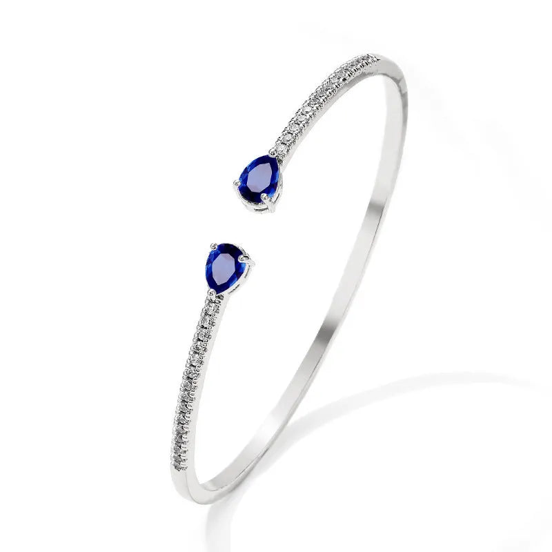 Close-up of a simple copper bracelet with inlaid blue zircon stones on a white background.