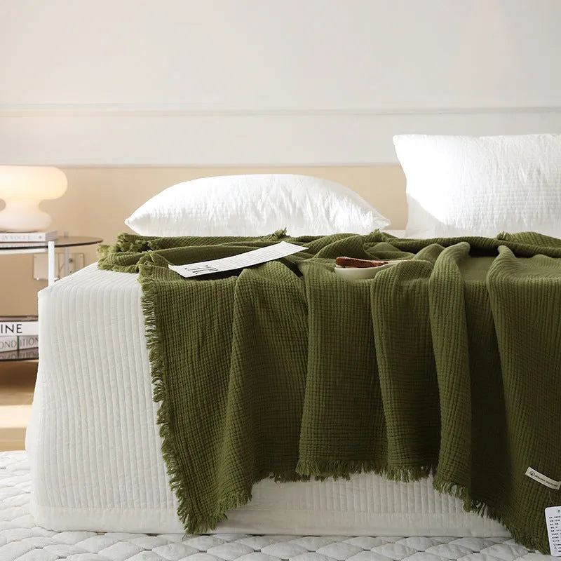 Four-layer cotton gauze blanket with tassel trim in avocado green colour laid flat.