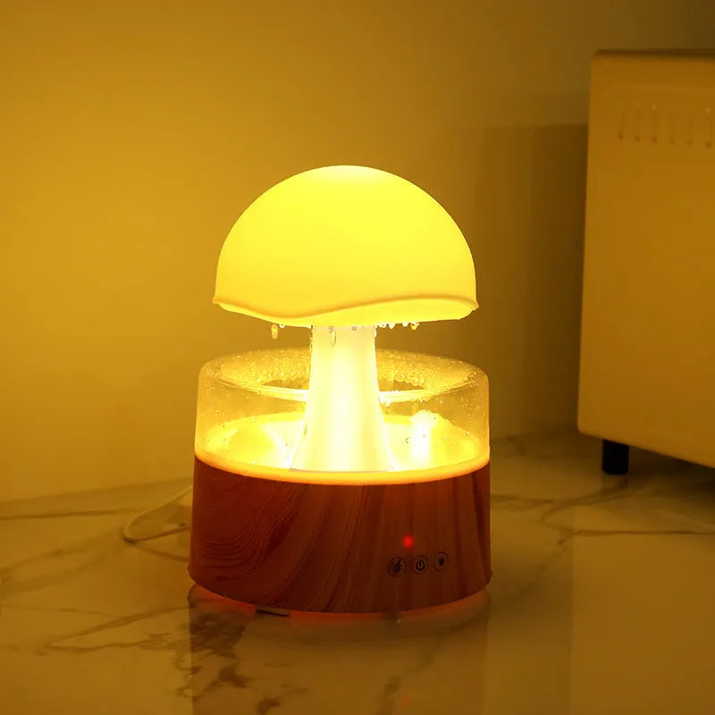White cloud-shaped humidifier on a table emitting mist and showing coloured LED lights inside, with a remote control beside it.