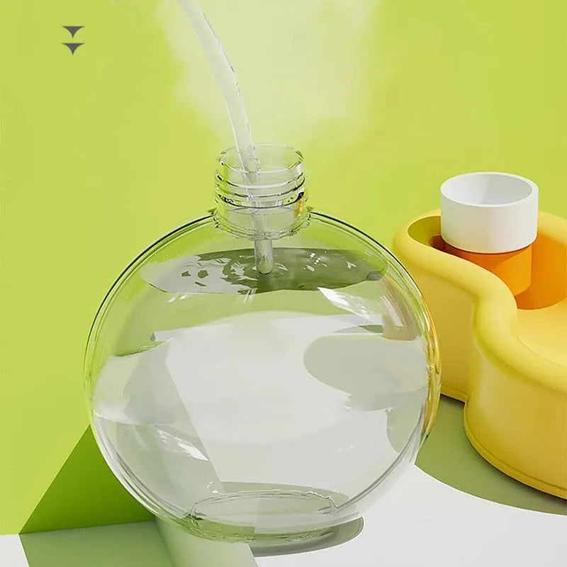 Green portable dog travel cup with pull-out bowl and handle, shown next to a backpack.