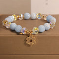 Women's aquamarine crystal bracelet with a four-leaf clover charm and pearl details on a white background