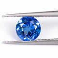 Royal blue cubic zirconia loose gemstone in a heart shape cut on a plain background.