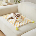 Green plaid patterned soft fleece pet blanket on a sofa, showing fur ball decoration.