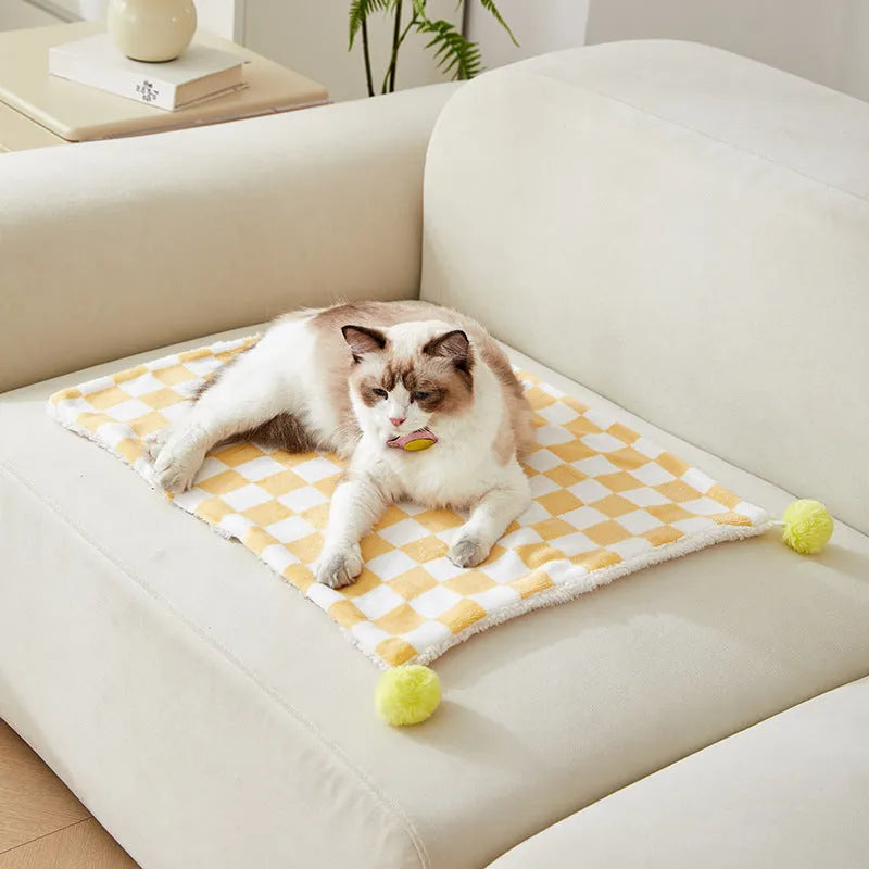 Green plaid patterned soft fleece pet blanket on a sofa, showing fur ball decoration.
