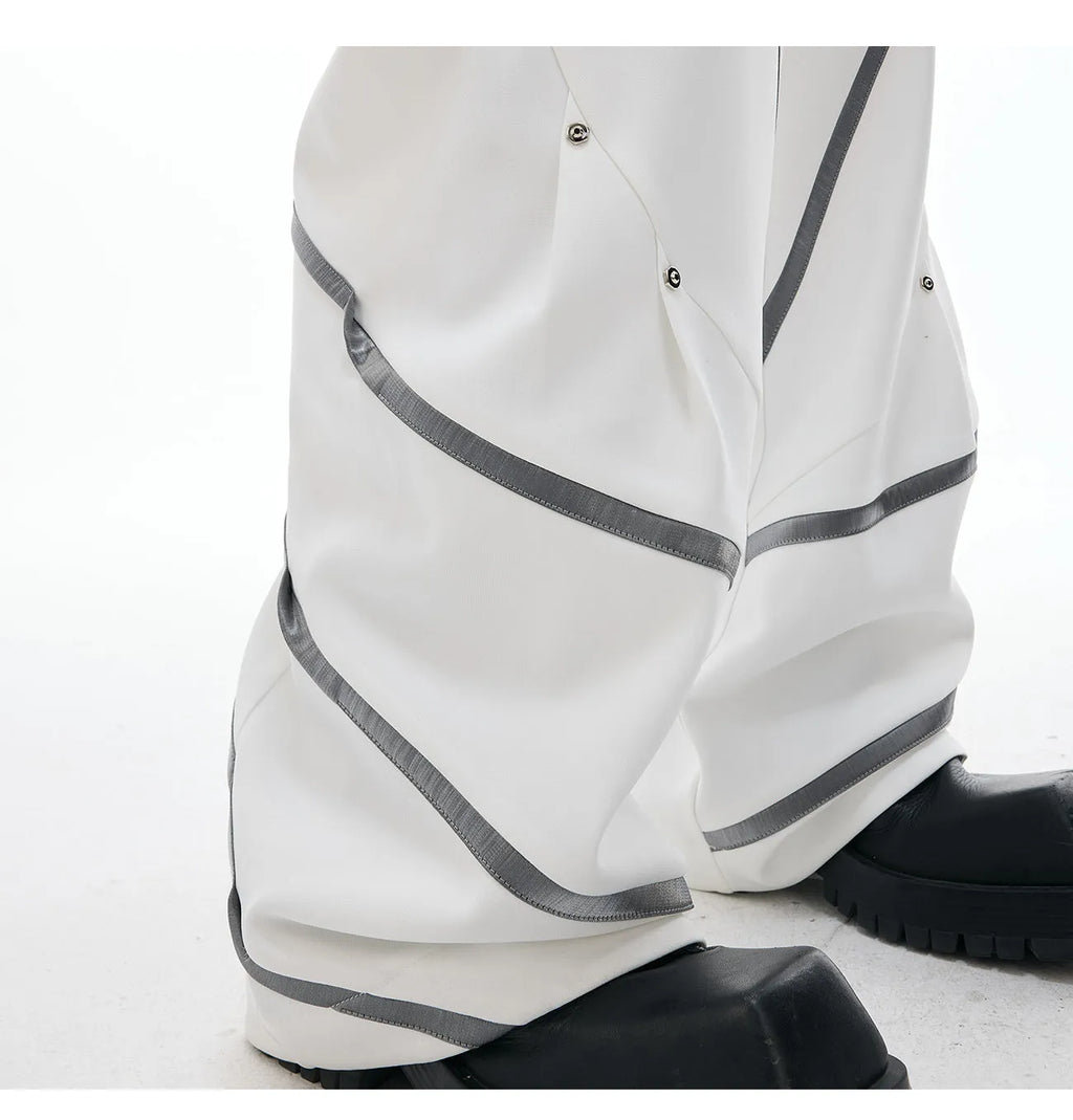 Men's black trousers with metal rivet pleats and a tapered leg, showing three-dimensional cutting.