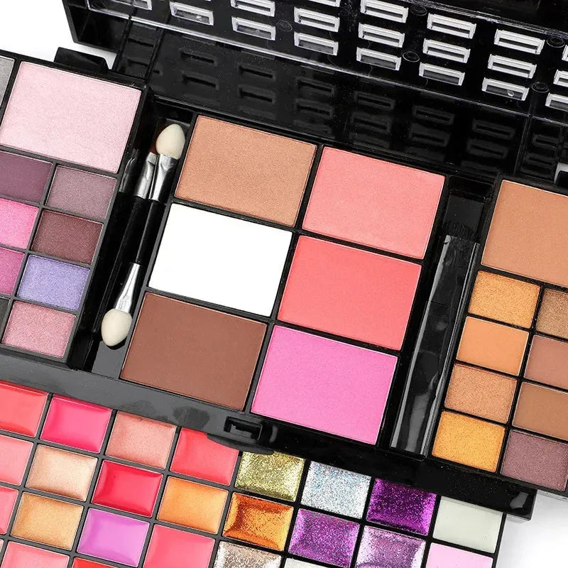 Open 74-colour makeup palette showing four layers of eyeshadow, lip gloss, blush, and contour powders with included brushes.