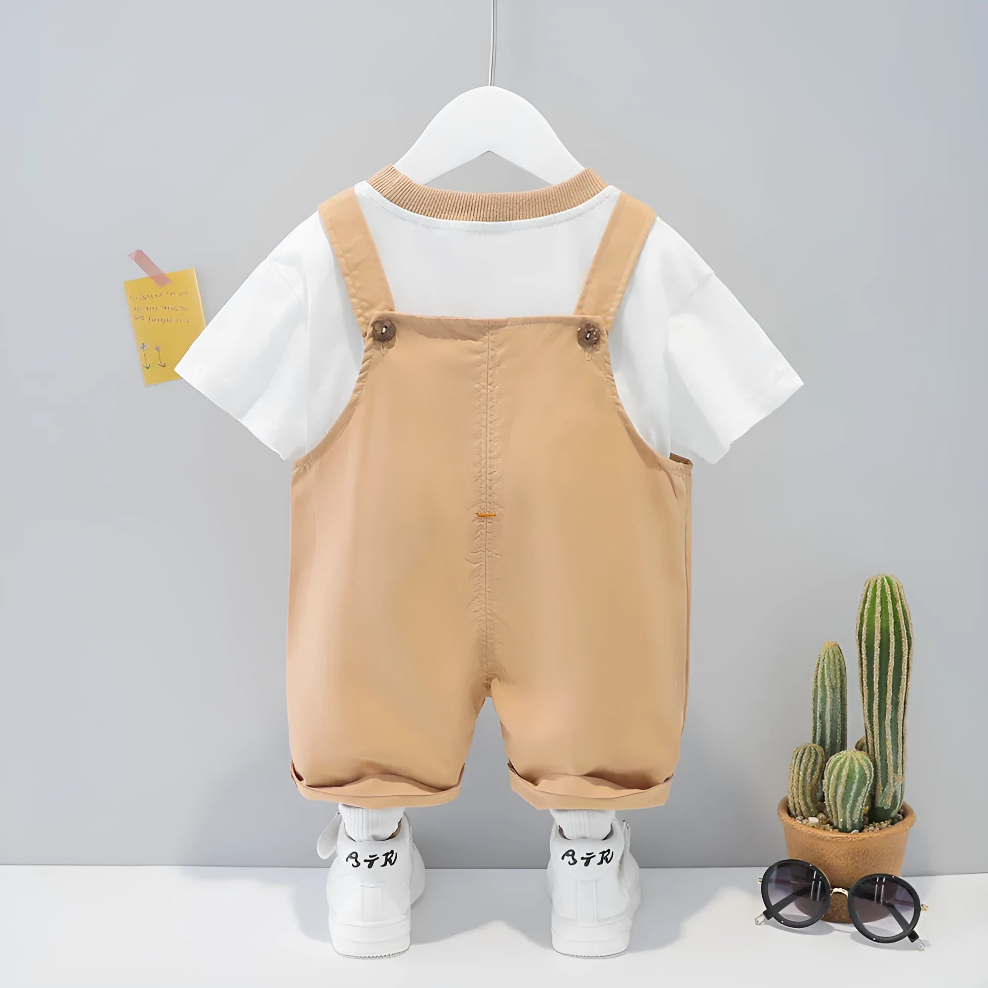 Yellow cartoon short-sleeved overalls for a baby on a hanger, showing the adjustable straps.