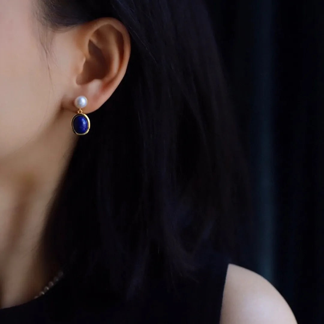 A pair of simple sterling silver stud earrings with blue lapis lazuli pearls and auspicious pattern details.