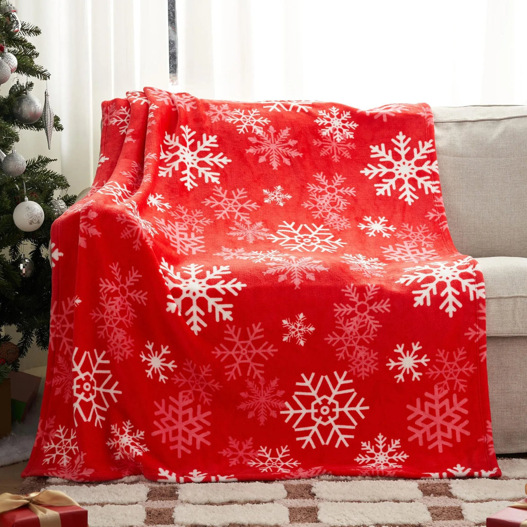 Soft red polyester flannel Christmas blanket with festive pattern draped over a bed