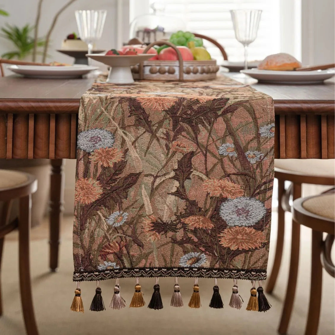 Beige jacquard table runner with long tassels and floral pattern laid on a wooden dining table.