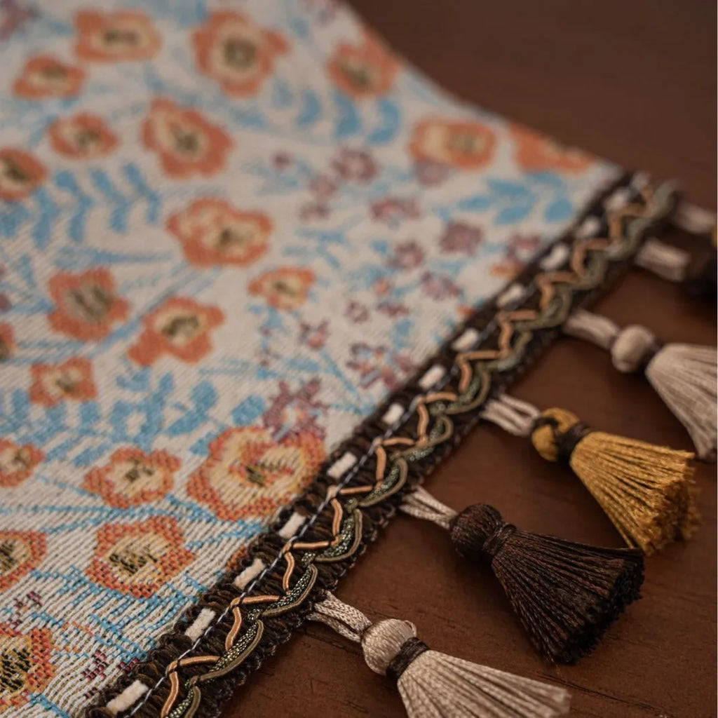 Beige jacquard table runner with long tassels and floral pattern laid on a wooden dining table.