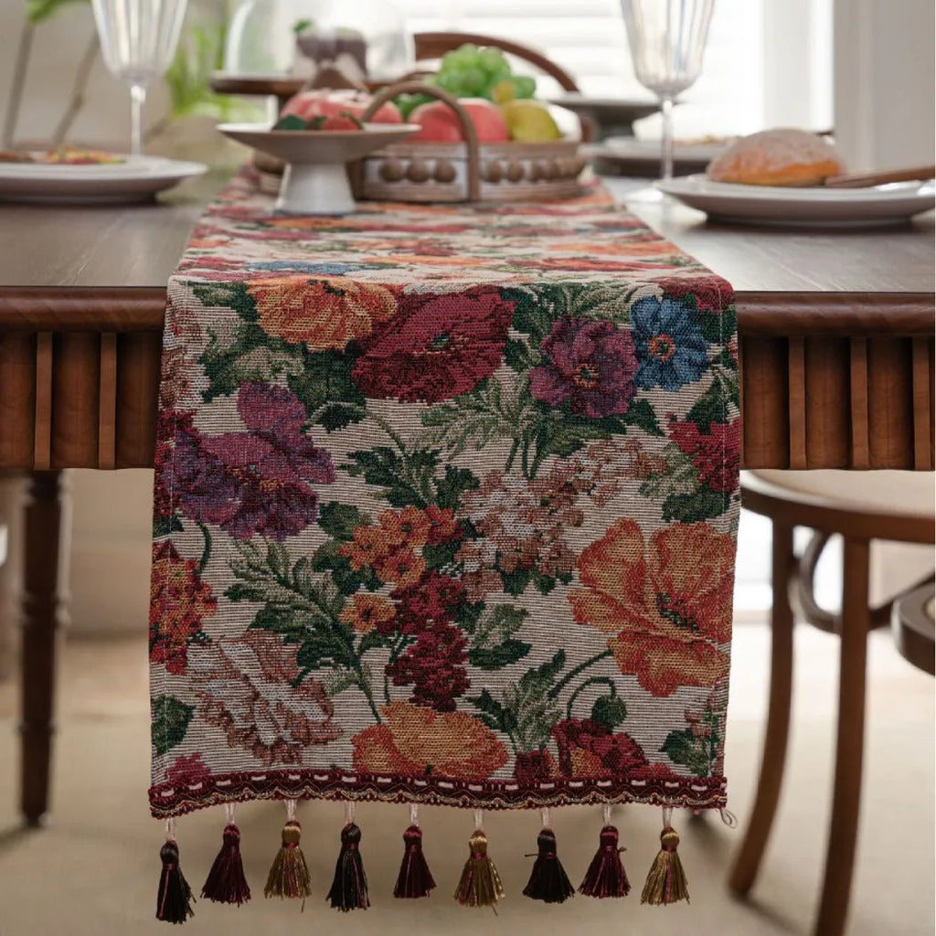 Beige jacquard table runner with long tassels and floral pattern laid on a wooden dining table.