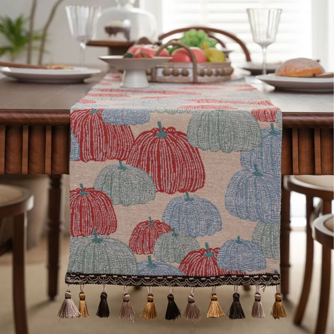 Beige jacquard table runner with long tassels and floral pattern laid on a wooden dining table.
