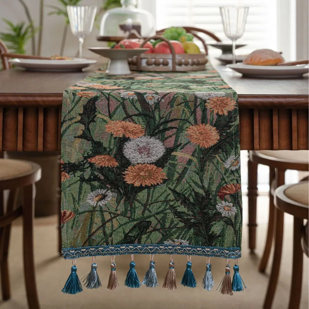 Beige jacquard table runner with long tassels and floral pattern laid on a wooden dining table.