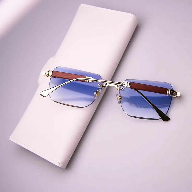 Frameless edge-cut sunglasses with gold frame, wood grain legs, and gradient grey lenses on a neutral background