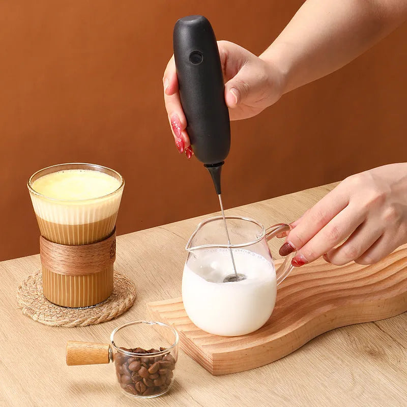 Black and white handheld electric milk frother with blending function on kitchen counter