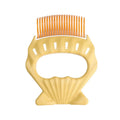 Green shell-shaped plastic pet grooming comb with bent wire bristles and an anti-slip handle.