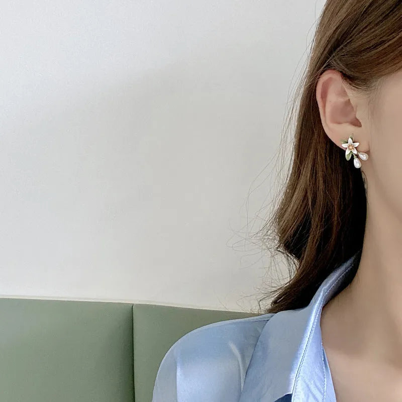 Close-up of women's camellia flower ear clip earrings with sterling silver needle accents on a contrasting background.