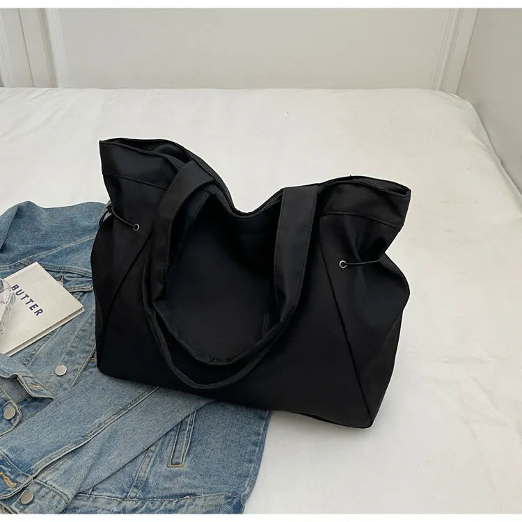 Soft Oxford cloth folding commuter tote bag shown in one of five colours: black, brown, dark grey, light grey or purple.