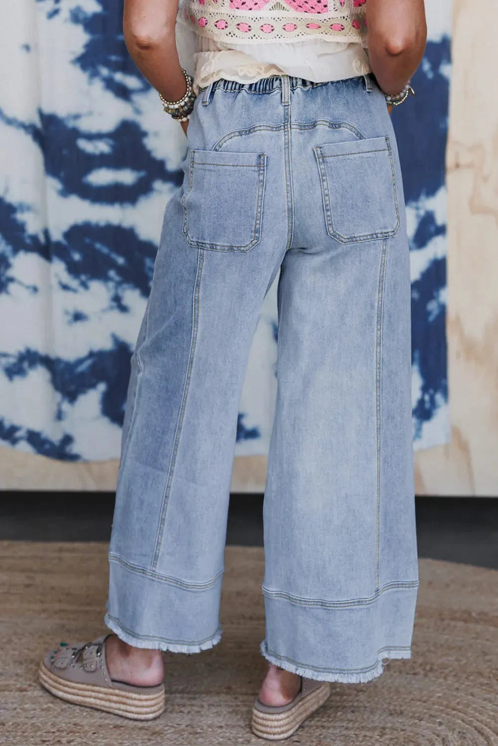 Beau blue wide leg denim pants on a hanger, showing drawstring waist and raw hem detail.